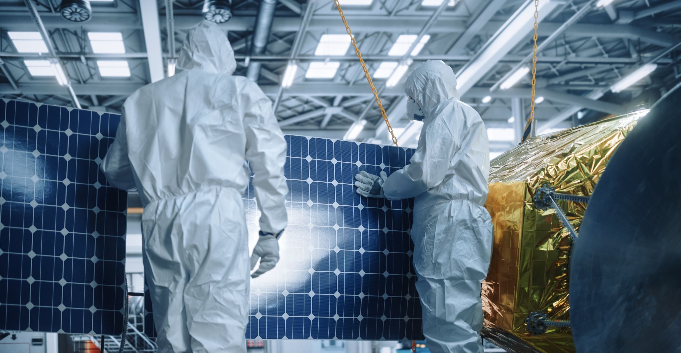 photo of solar cells in the backgroud and two people wearing hazmat suits with face masks in the foreground
