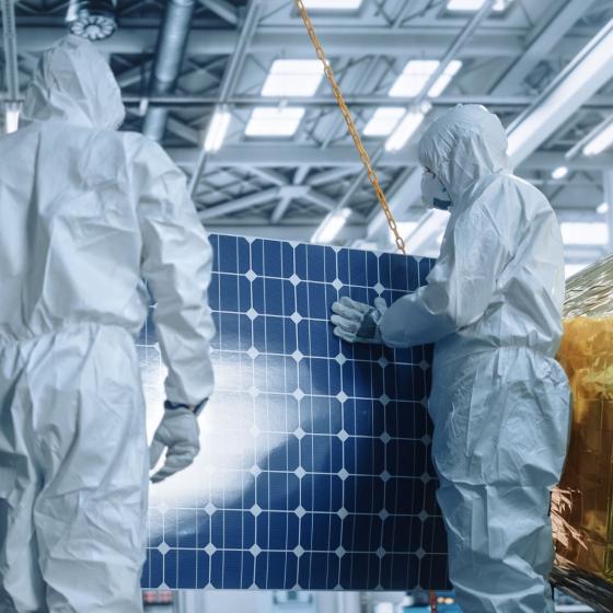 photo of solar cells in the backgroud and two people wearing hazmat suits with face masks in the foreground